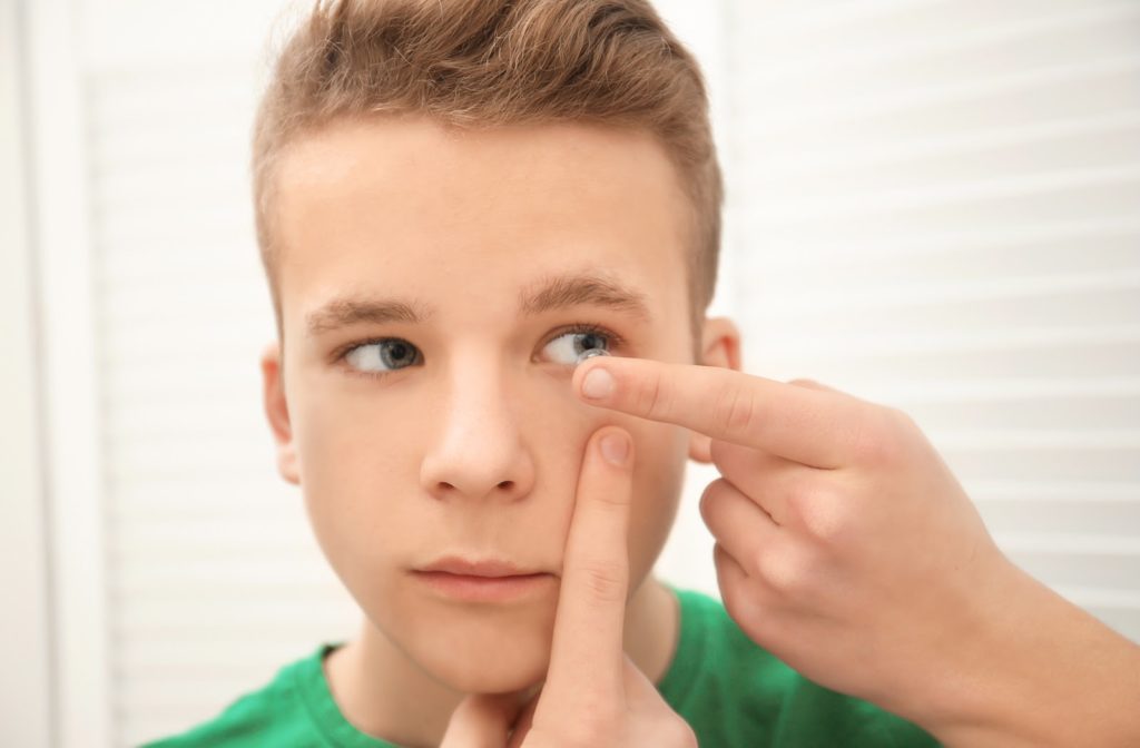 Young boy putting in ortho-k lenses while holding eye open with fingers.