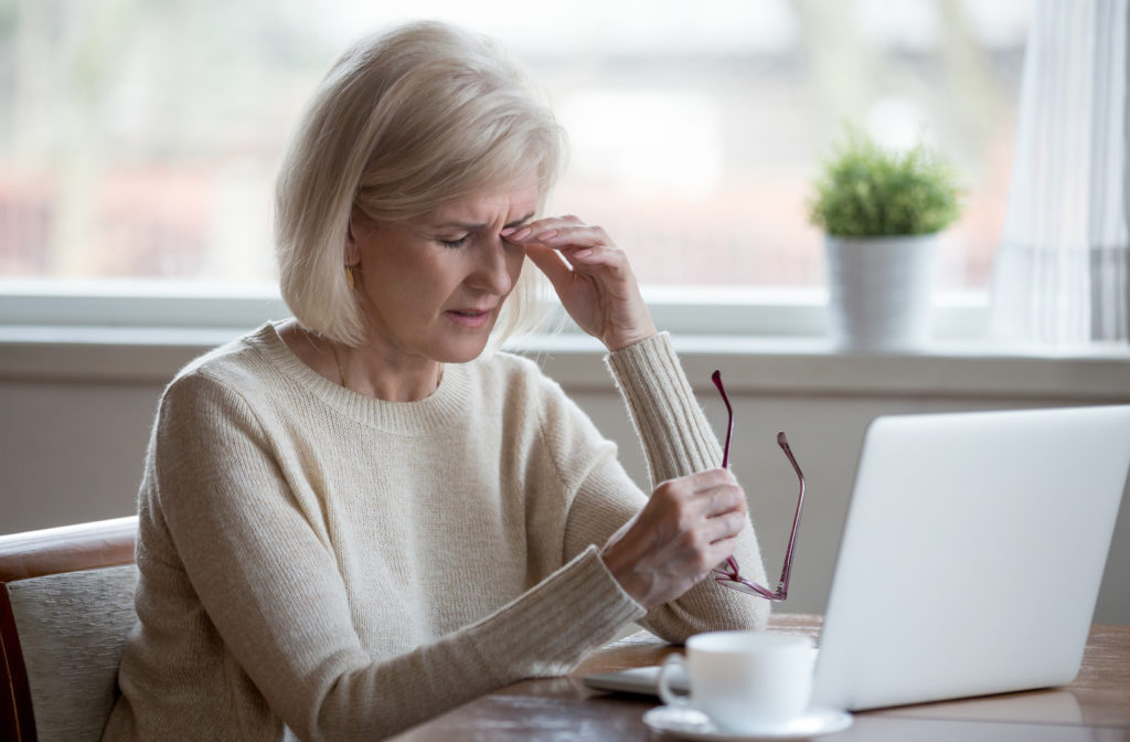 Women experiencing dry eye symptoms while working on laptop and taking off glasses for some comfort