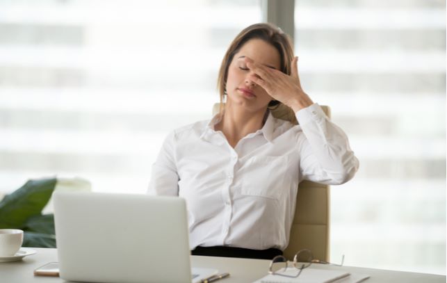 women experiencing dry eye and touching eye for comfort while working in office sitting