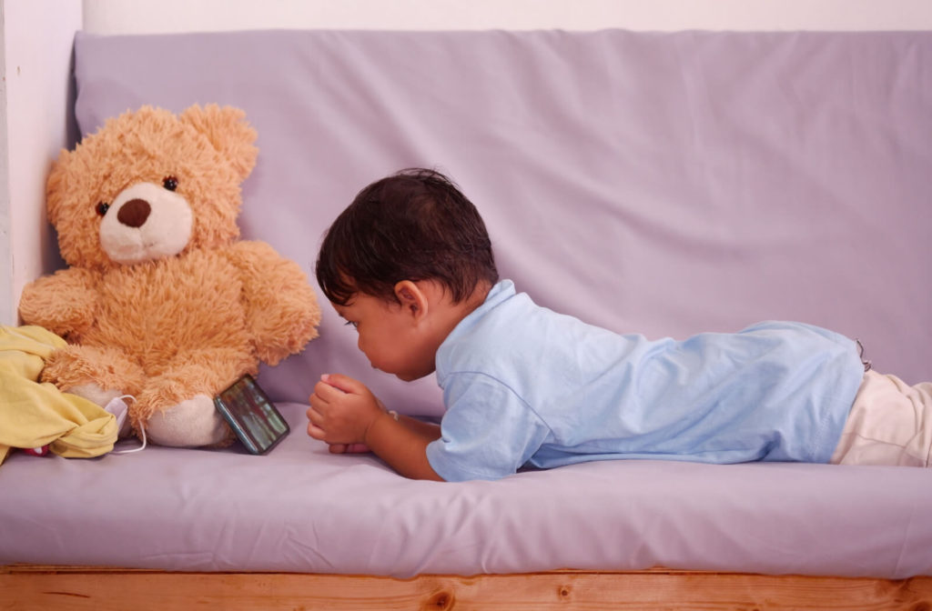 A two year old male child in a prone position watching a video on a smartphone.
