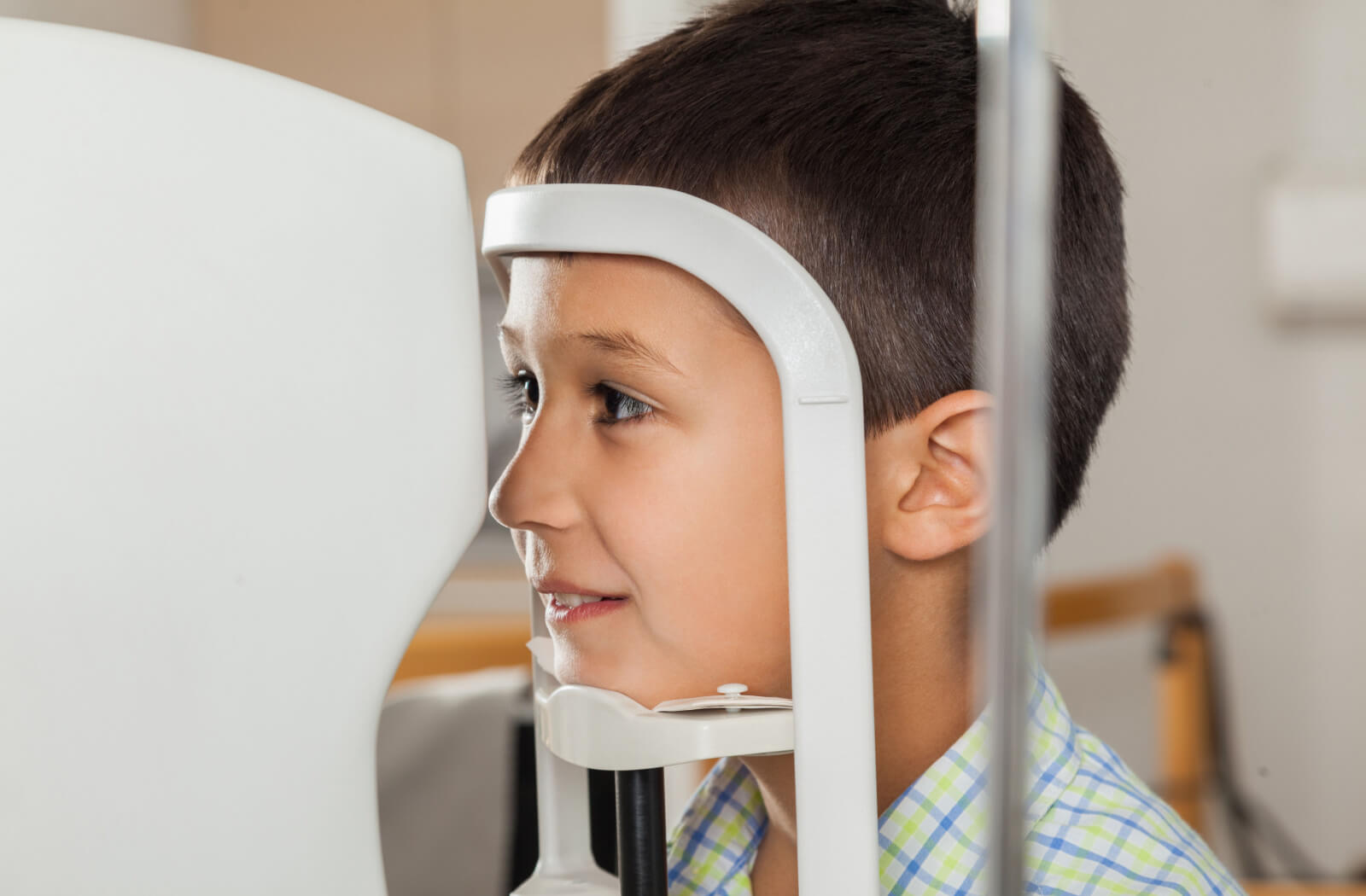 A boy sitting in front of an autorefractor machine at the ophthalmologist clinic getting his regular eye test.