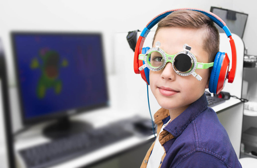 A boy wearing special eyewear covering his left eye and wearing a blue and red colored headset while undergoing treatment for Amblyopia in front of a computer.