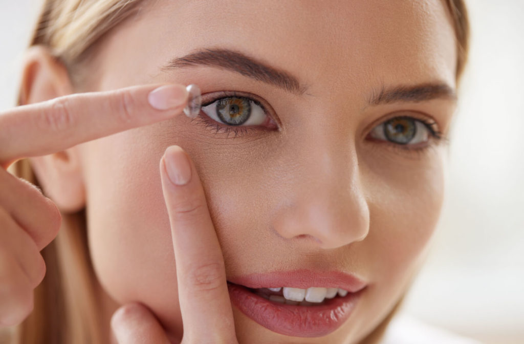 A woman using her left index finger to pull her eyelid down while she puts a contact lens on her right eye with her right hand