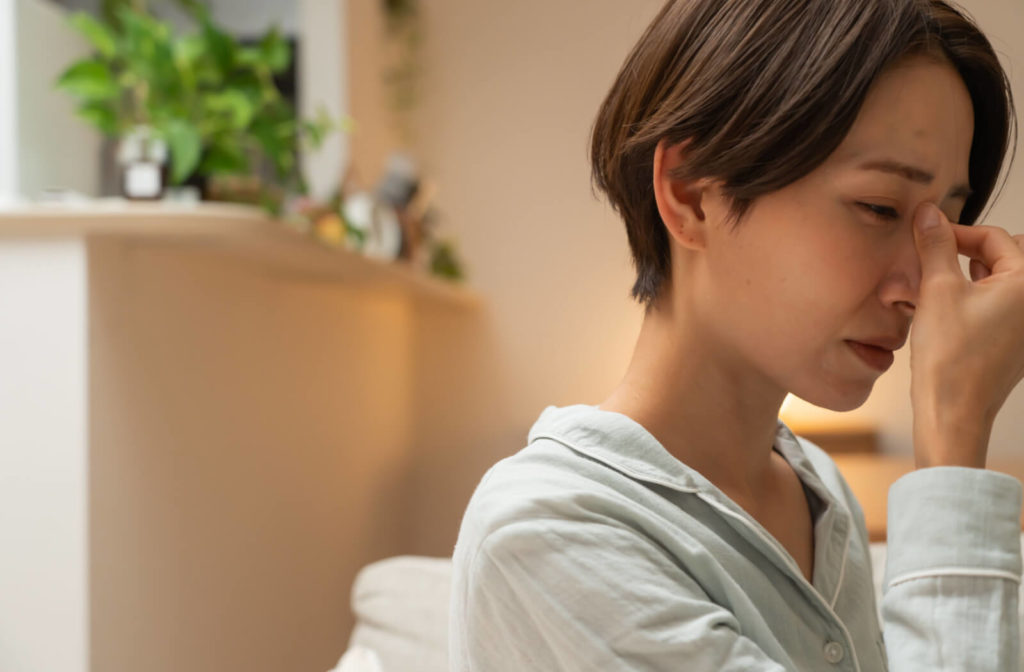 A woman wearing pajamas with dry eyes is pressing her nasal bridges