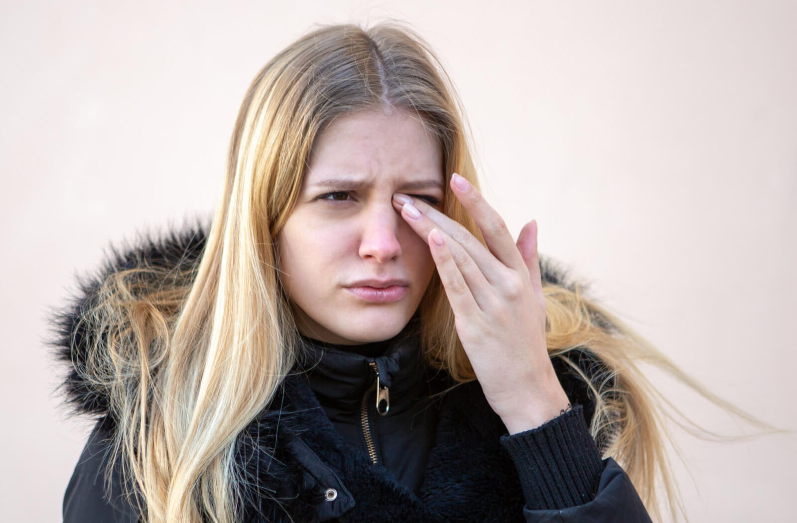 A young woman in a winter coat rubbing her left eyes with her left hand