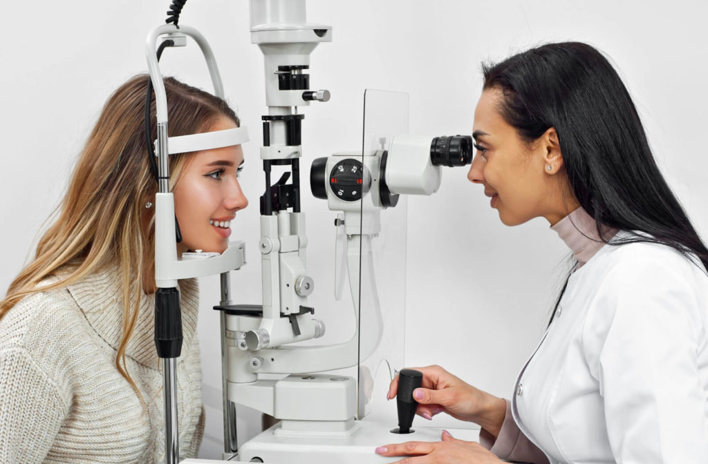 A female optometrist examining the eyes of a young woman using a medical device to detect potential eye problems.