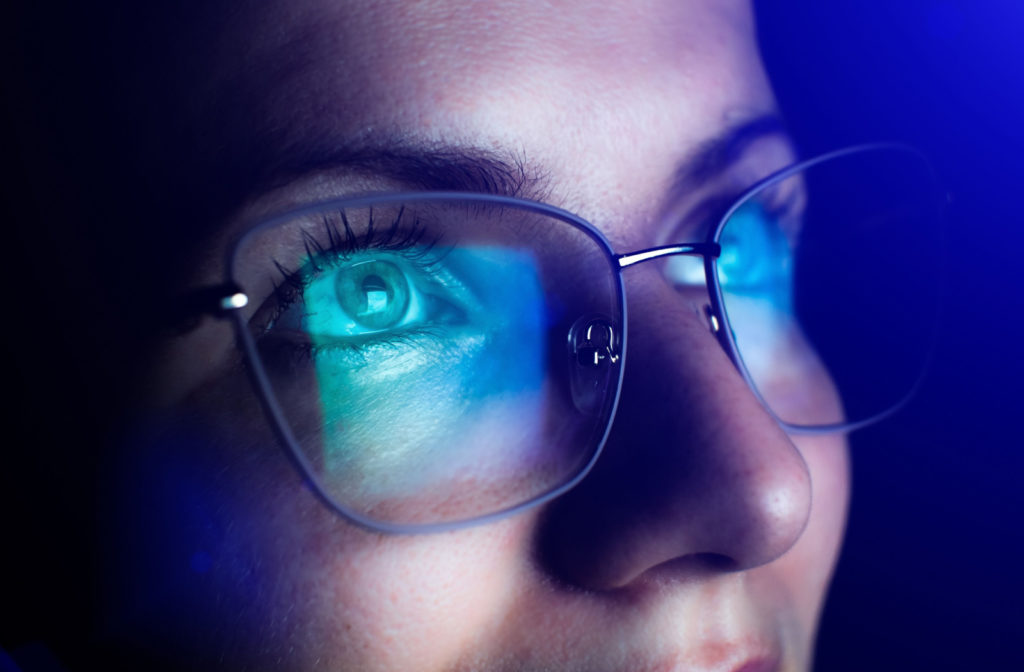 A woman with blue light reflected on her glasses from a screen.