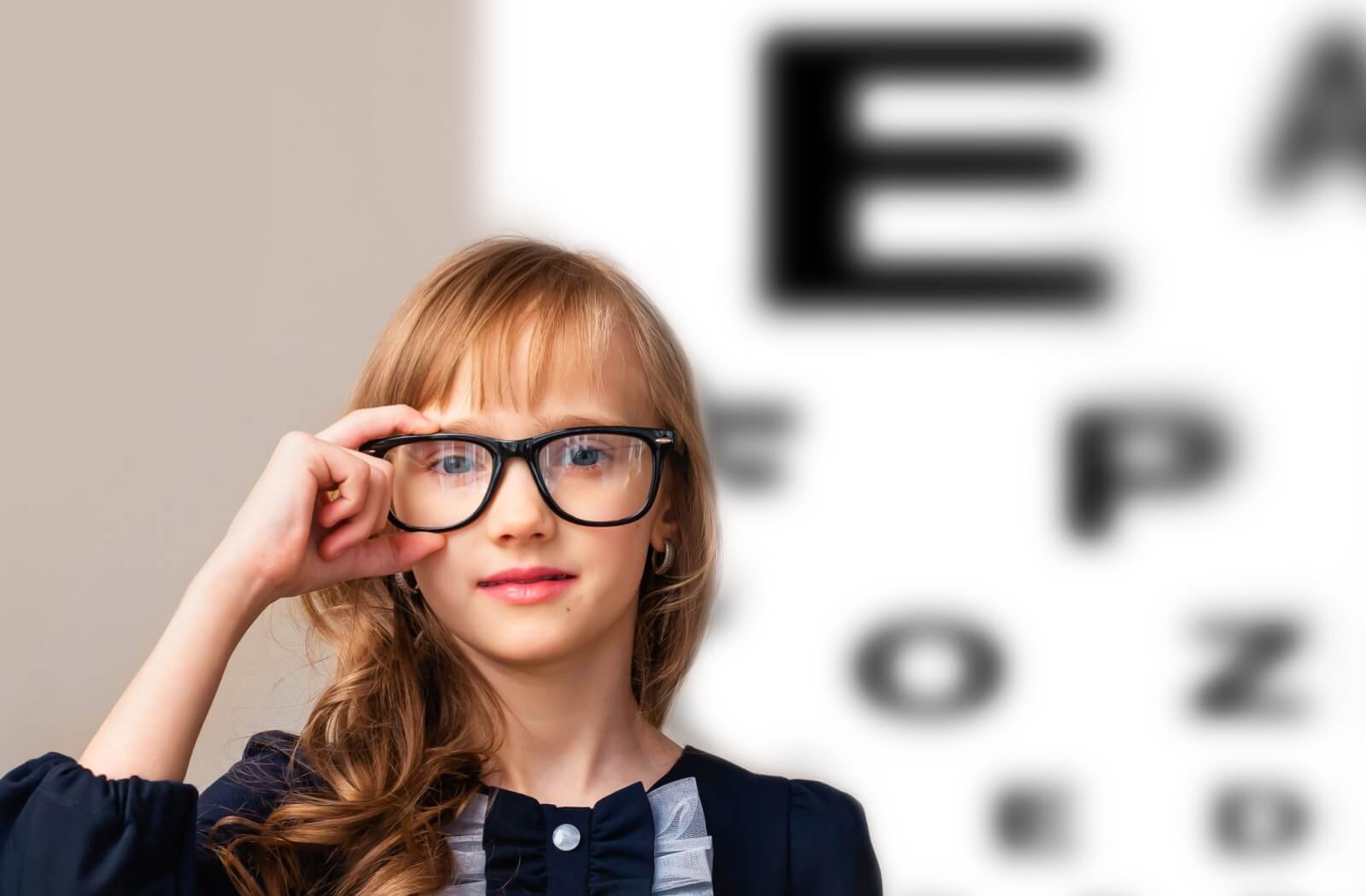 A child delicately holds black-framed glasses to their eyes.