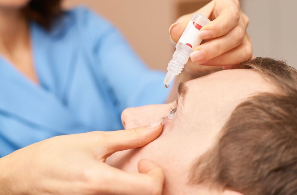 An optometrist is treating a patient's dry eye by squeezing eye drops into their eye.