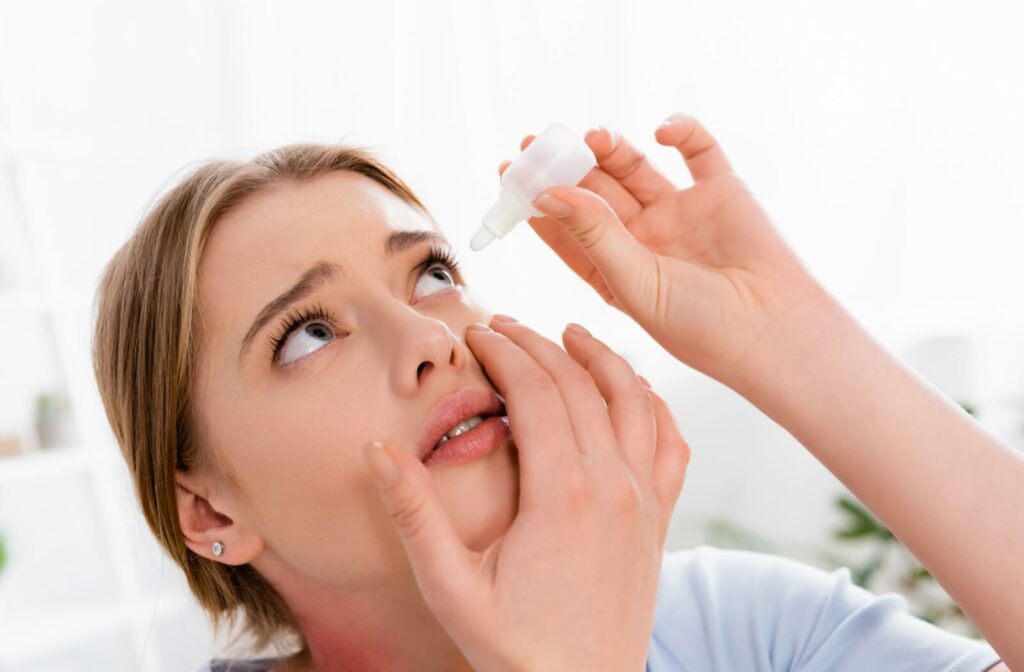 A person applies eye drops to their eyes with an apprehensive look.