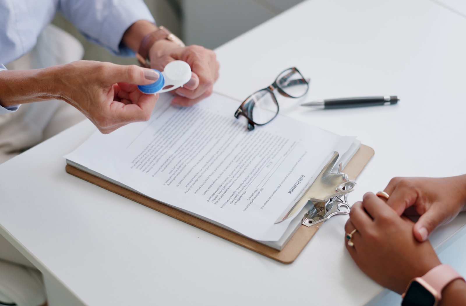 A close-up image of an optometrist handing over a pair of contact lenses to a patient after their eye exam.