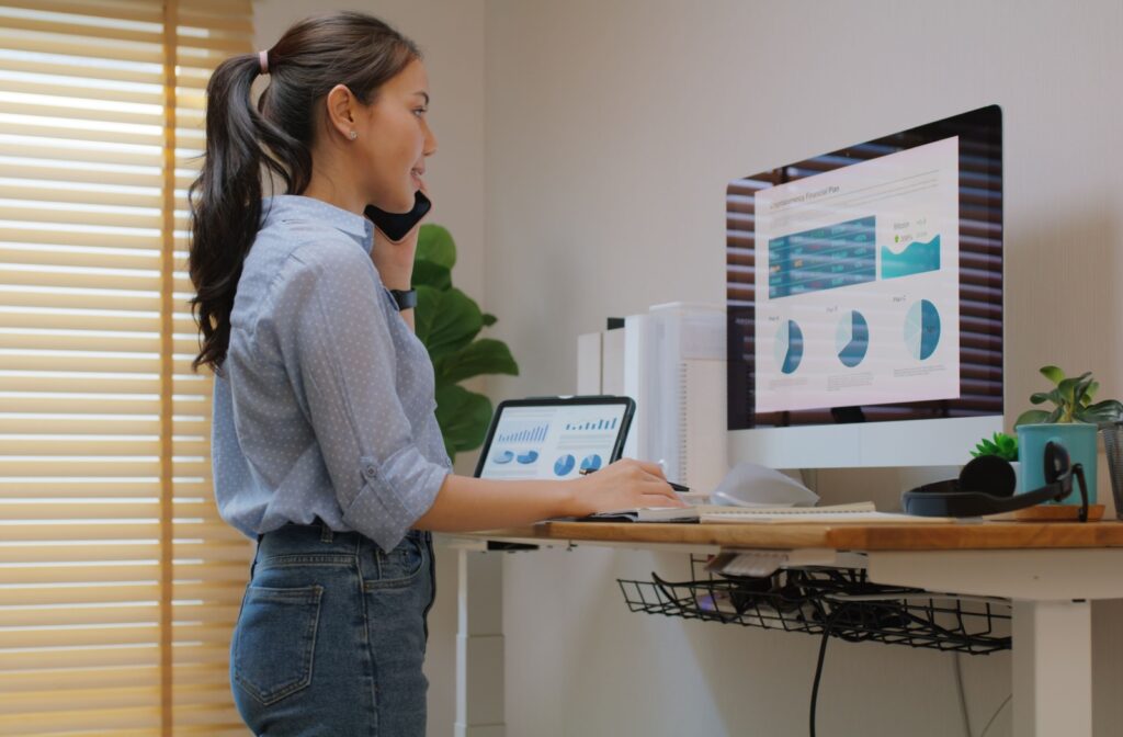 An office worker uses a standing desk for better posture while using screens to alleviate shoulder pain and eye strain.