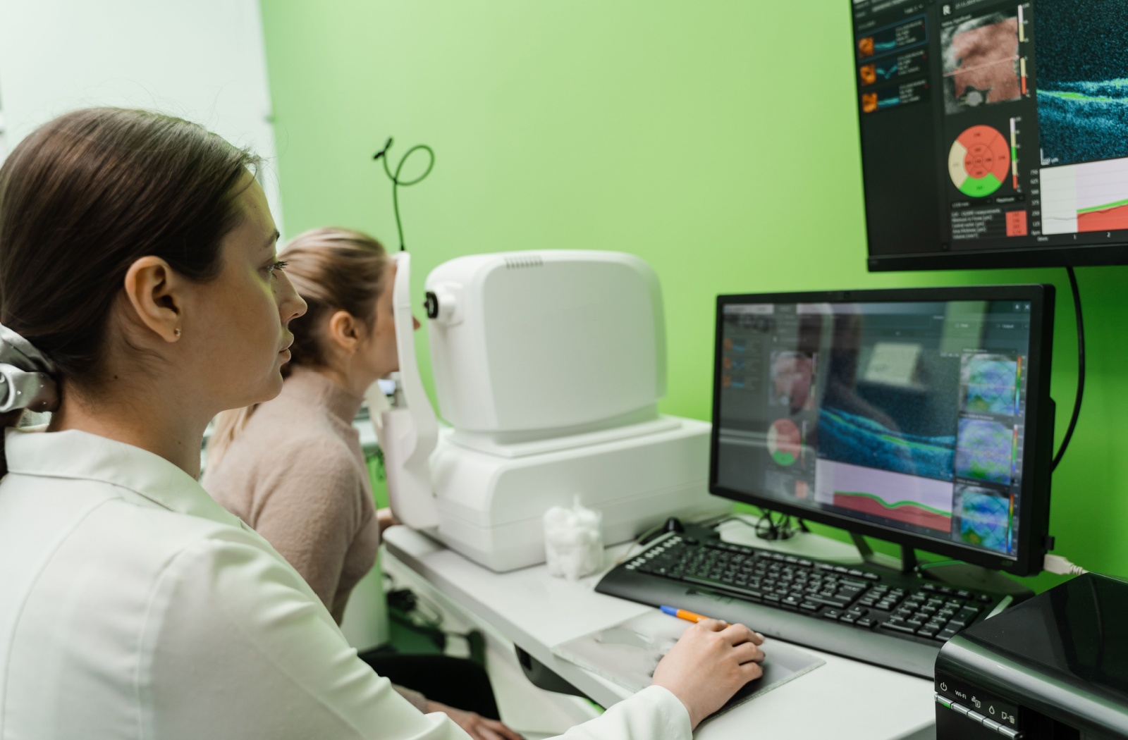 An optometrist uses an optical coherence tomography (OCT) eye scan with a patient to take pictures of the back of their eyes.