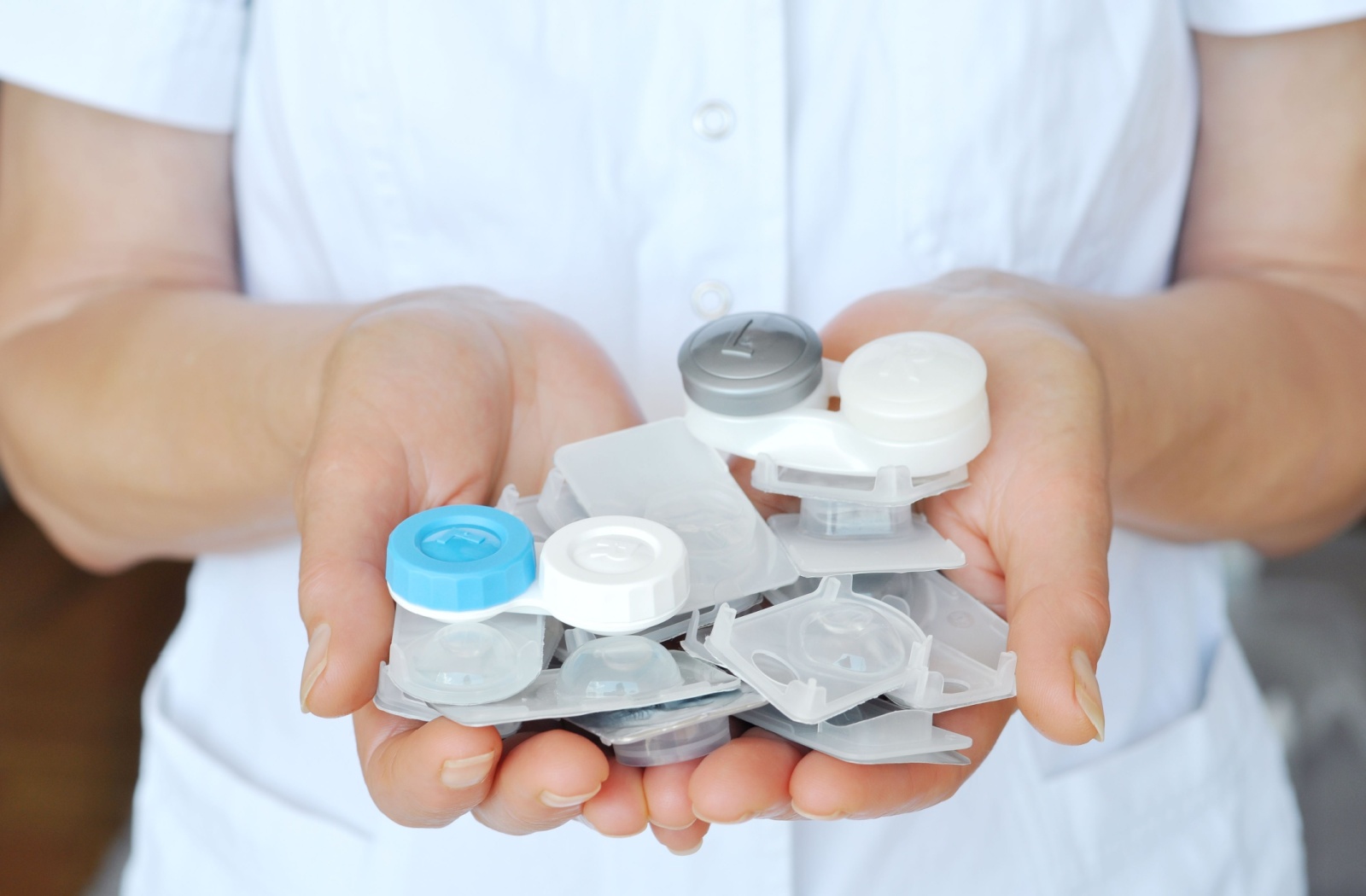A person holding multiple contact lens cases and packaging in their hands.