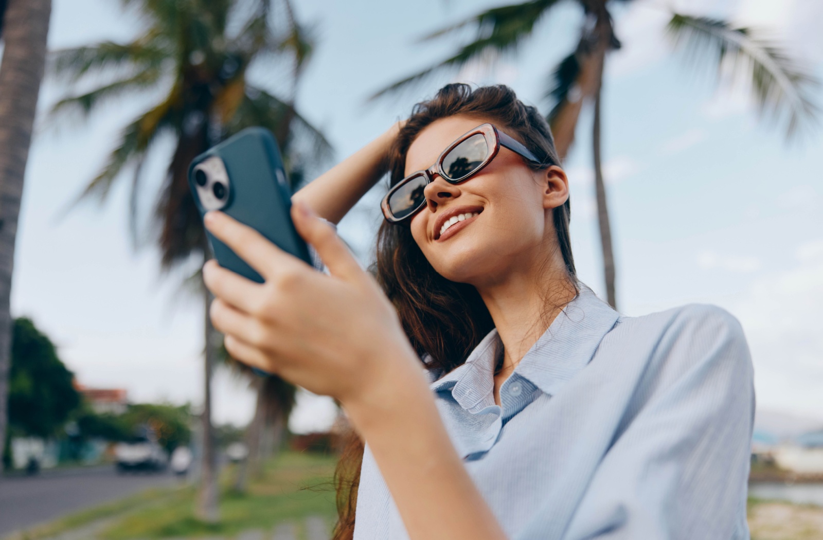 Someone wearing prescription sunglasses takes a photo on their phone on a sunny day.